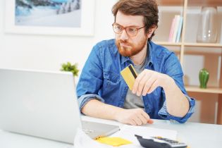 Mężczyzna siedzi przed komputerem trzymając kartę kredytową