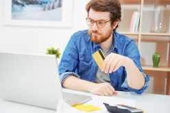 Mężczyzna siedzi przed komputerem trzymając kartę kredytową