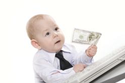 małe dziecko opadre na klawiaturze z banknotem dolarowym w ręku